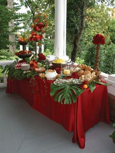 a table covered with food and flowers on the outside porch, in front of some trees