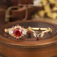 two gold rings with red and white stones on top of a wooden table next to a vase