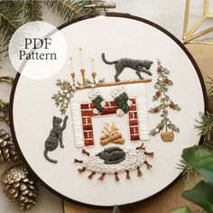 a cross stitch pattern with two cats and a fireplace in the center, surrounded by pine branches