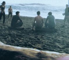 a group of people sitting on top of a sandy beach