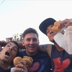 three men eating hamburgers while standing next to each other