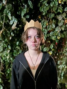 a woman with a crown on her head standing in front of some bushes and trees