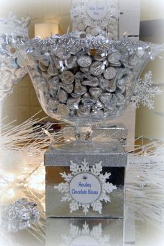 a glass bowl filled with silver candies on top of a table next to snowflakes