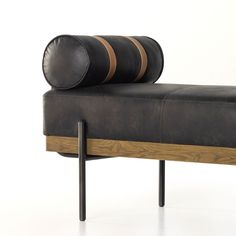 a black leather bench with two wooden barrels on it's back end and legs