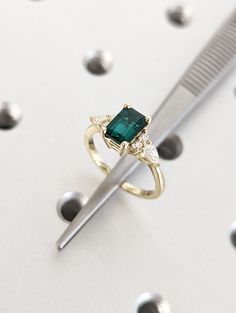 a diamond and emerald ring sitting on top of a table next to a toothbrush