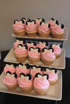 cupcakes with pink frosting and mickey mouse ears on top are arranged in three tiers