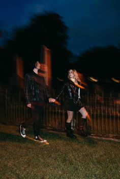 a man and woman holding hands while standing in front of a fence at night time