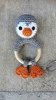 a knitted penguin ring rattler sitting on top of a wooden surface with an orange nose