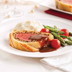 a white plate topped with meat and veggies next to mashed potatoes, asparagus and tomatoes