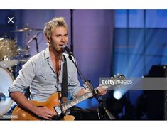 a man holding a guitar and singing into a microphone on the set of american idol