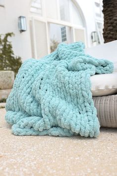 a blue blanket laying on top of a bed next to pillows and pillow cases in front of a house