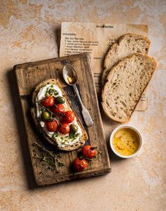 an open face sandwich with tomatoes and olives on a cutting board next to bread