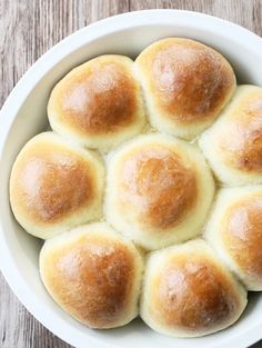 a white bowl filled with rolls on top of a wooden table