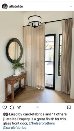 an image of a room with curtains and a table in front of the door that has a mirror on it