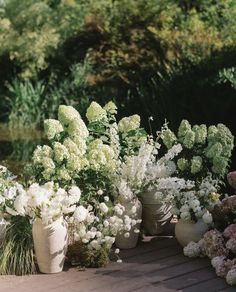 several vases filled with white flowers sitting on a wooden deck next to some bushes