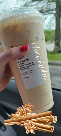 a woman holding up a cup of coffee with cinnamon sticks on the side of it