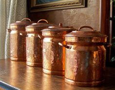 copper pots and pans are lined up on a shelf in front of a painting