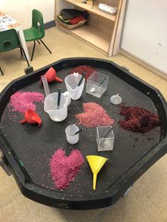 there are many cups and spoons in the tray on the table, with different colored sand