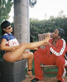 a woman in red pants sitting on a chair next to a man with his foot up