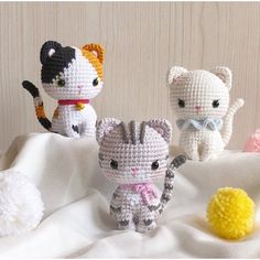 three crocheted kittens sitting on top of a white blanket next to a yellow ball