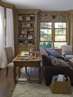 a living room filled with furniture and a wooden table in front of two large windows