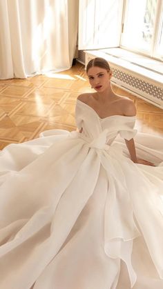 a woman is sitting on the floor in a white wedding dress with ruffles