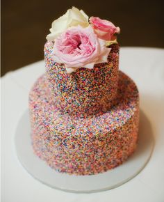 a three tiered cake with sprinkles and flowers on top