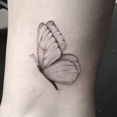 a black and white butterfly tattoo on the ankle, with one wing extended to the side