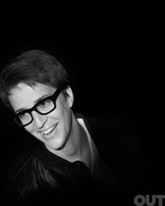 black and white photograph of a man with glasses smiling at the camera in front of a dark background