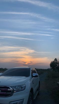 a white car is parked on the side of the road at sunset or dawn with clouds in the sky