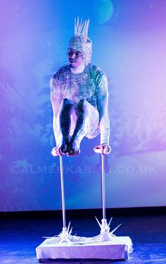 a man is performing on stilts in front of a blue background and purple lighting