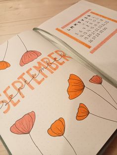 an open planner with orange flowers and the word september written on it is sitting on a wooden table