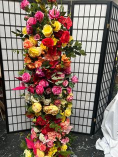 a tall vase filled with lots of different colored flowers next to a white screen wall