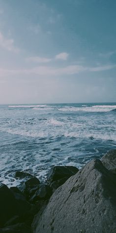 an ocean view with waves coming in from the water and rocks on the shore, under a cloudy blue sky