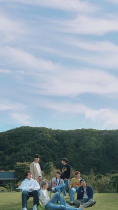 a group of people sitting on top of a lush green field under a blue sky