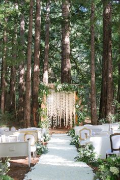 an outdoor ceremony in the woods with white linens and greenery on the aisle