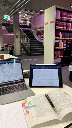 two laptops sitting on top of a table next to an open book and pen