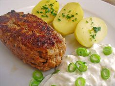 a white plate topped with meat, potatoes and green onions next to sour cream sauce