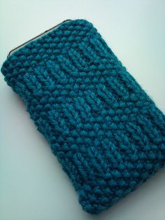 a blue crocheted purse sitting on top of a white table next to a cell phone