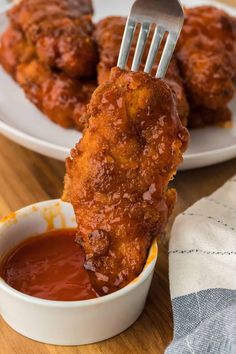 a fork is lifting up some deep fried chicken wings from a small white bowl with ketchup