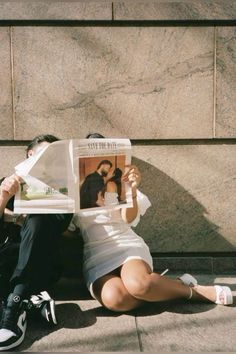 a man and woman sitting on the ground reading a newspaper with their feet up in the air