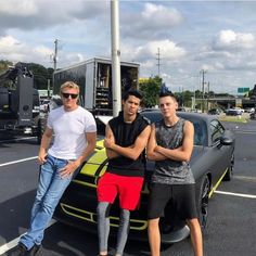 three young men standing next to a yellow and black sports car in a parking lot