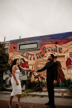 a man standing next to a woman in front of a mural