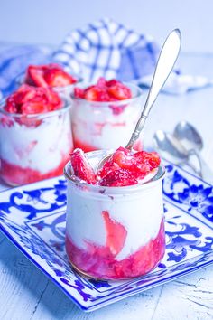 two small desserts with strawberries in them on a blue and white plate next to a spoon