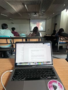 an open laptop computer sitting on top of a wooden desk in front of a class room