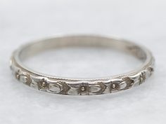 an antique silver wedding band with flowers and leaves on the side, sitting on a white surface