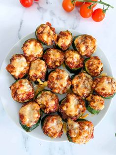 some stuffed peppers are on a white plate with tomatoes and basil leaves next to them