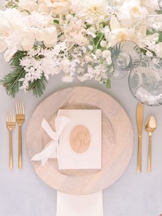 a place setting with white flowers and gold cutlery, napkins and silverware