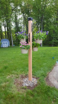 a wooden pole with potted plants on it in the middle of a grassy area