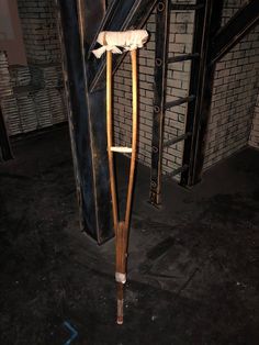 an old wooden walking stick leaning against a brick wall in a basement with exposed piping